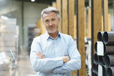 Portrait of a confident mature businessman in a factory storehouse with steel pipes - MOEF03078