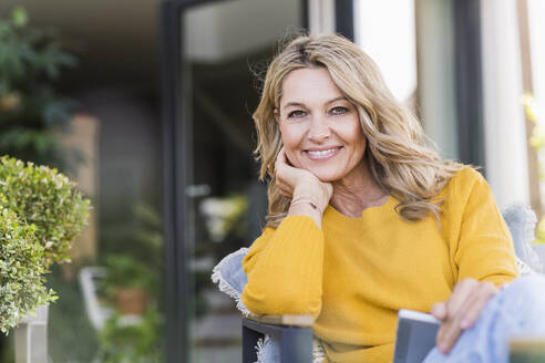 Portrait of happy mature woman sitting on terrace with digital tablet - UUF20533