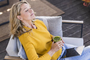 Porträt einer reifen Frau auf der Terrasse sitzend mit digitalem Tablet und einem Glas Smoothie - UUF20540