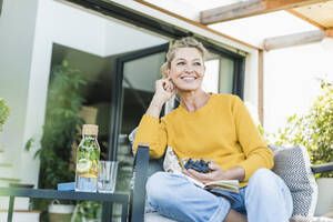 Porträt einer glücklichen reifen Frau, die sich auf einer Terrasse entspannt - UUF20544