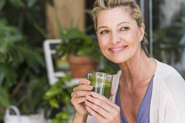 Portrait of smiling mature woman with enjoying green smoothie - UUF20569