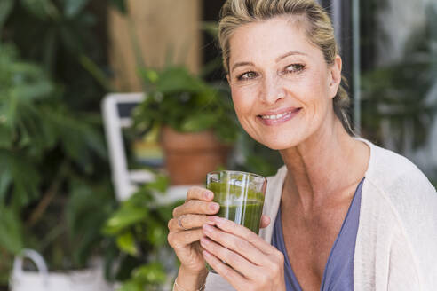 Porträt einer lächelnden reifen Frau, die einen grünen Smoothie genießt - UUF20569