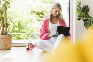 Porträt einer reifen Frau, die zu Hause auf dem Boden sitzt und ein digitales Tablet benutzt - UUF20629