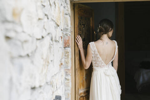 Rückansicht einer Frau im eleganten Hochzeitskleid an der Tür, lizenzfreies Stockfoto