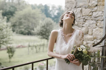 Junge lächelnde Frau in elegantem Hochzeitskleid mit Blumenstrauß - ALBF01280
