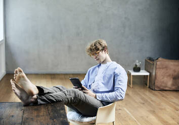 Young man with feet on table using digital tablet - FMKF06202