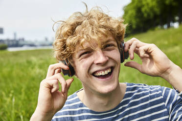 Lachender junger Mann, der mit Kopfhörern Musik hört - FMKF06211