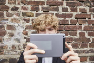 Blonder junger Mann macht Selfie mit digitalem Tablet im Freien - FMKF06215