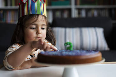 Porträt eines kleinen Mädchens, das einen Geburtstagskuchen berührt - VABF03018