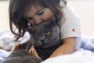 Little girl cuddling grey cat on bed - VABF03030