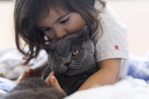 Kleines Mädchen kuschelt mit grauer Katze auf dem Bett - VABF03030