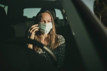 Mittlere erwachsene Frau mit Schutzmaske benutzt Smartphone im Auto - DMGF00091