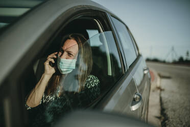 Mid adult woman with protective mask using smartphone in car - DMGF00092