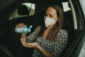Mid adult woman with protective mask using sanitizer in car - DMGF00103