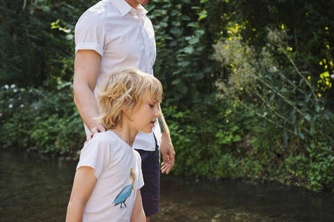 Father and son walking in stream during sunny day at forest stock photo