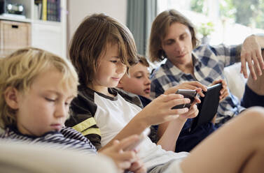 Vater schaut auf Jungen, die im Wohnzimmer Spiele auf Smartphones und Tablets spielen - PWF00127
