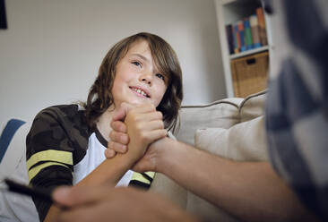 Lächelnder Junge beim Armdrücken mit seinem Vater auf dem Sofa im Wohnzimmer - PWF00130