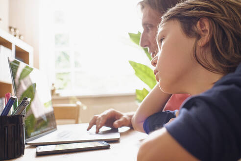 Vater und Sohn benutzen einen Laptop, während sie zu Hause lernen - PWF00135