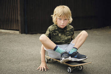 Cute boy sitting on skateboard at yard - PWF00144