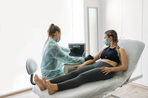 Doctor wearing face mask examining sportswoman with ultrasound scanner stock photo