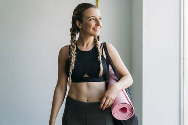 Sportliche Frau trägt Tasche mit Gymnastikmatte im Fitnessstudio - MPPF00940