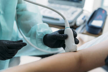 Arzt in Schutzkleidung untersucht den Arm einer Frau mit einem Ultraschallgerät - MPPF00942