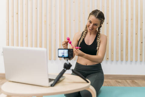 Sporty woman filming herself with camera and laptop introducing a product stock photo