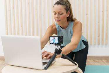 Sportliche Frau filmt sich selbst mit Kamera und Laptop - MPPF00948
