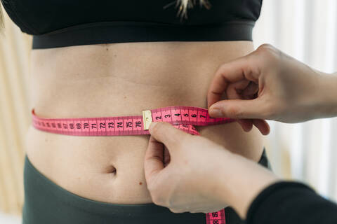 Fit and healthy young lady measuring her waist with a tape measure