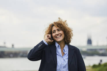 Geschäftsfrau mit Smartphone am Flussufer in Köln, Deutschland - MJFKF00321