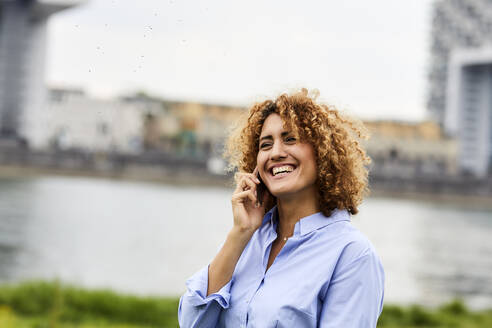 Geschäftsfrau mit Smartphone am Flussufer in Köln, Deutschland - MJFKF00327