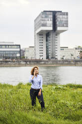 Businesswoman using smartphone at riverside in Cologne, Germany - MJFKF00329