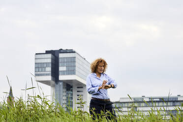 Geschäftsfrau beim Prüfen der Uhrzeit, im Hintergrund das Kranhaus, Köln, Deutschland - MJFKF00331