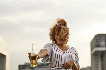 Portrait of smiling woman with glass bottle outdoors - MJFKF00344