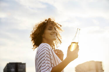 Portrait of smiling woman with glass bottle outdoors - MJFKF00354