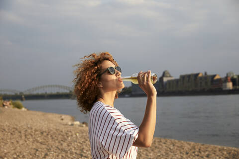 Porträt einer lächelnden Frau mit Glasflasche am Flussufer, lizenzfreies Stockfoto