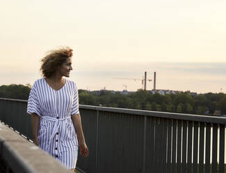 Portrait of smiling woman walking on bridge in the evening - MJFKF00361
