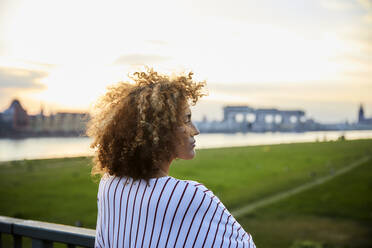 Rückansicht einer Frau, die die Aussicht von der Brücke im Abendlicht genießt - MJFKF00362