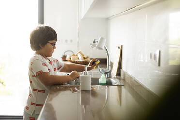 Boy washing dishes at home - VABF03034