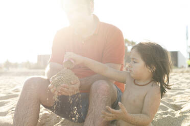 Vater spielt mit seiner Tochter und Sand am Strand - VABF03045