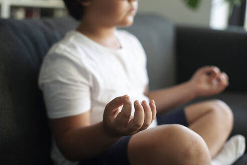 Boy sitting on couch meditating - VABF03048