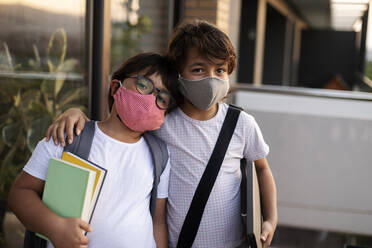 Siblings with books wearing masks outdoors - VABF03059