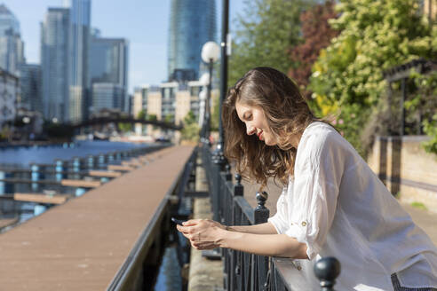 Junge Frau lehnt sich mit ihrem Smartphone an das Geländer der Promenade - WPEF03002