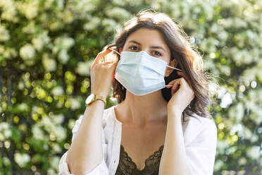 Young woman putting on protective mask outdoors - WPEF03004