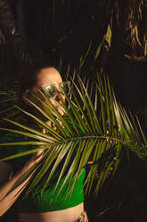 Woman with sunglasses hiding behing palm leaves - ERRF04005