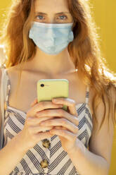 Nahaufnahme einer jungen Frau mit Gesichtsmaske, die ein Smartphone benutzt - AFVF06611