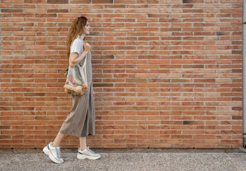 Side view of stylish young Asian woman walking at metal wall. stock photo