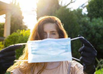 Close-up of woman holding mask against trees in yard - AFVF06626