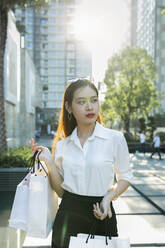 Selbstbewusste junge Frau mit Einkaufstüten in der Hand in der Stadt stehend - JPTF00527