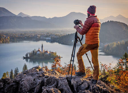 Slowenien, Oberkrain, Bled, Mann fotografiert die Insel Bled und die Wallfahrtskirche Mariä Himmelfahrt bei nebligem Morgengrauen - HAMF00635